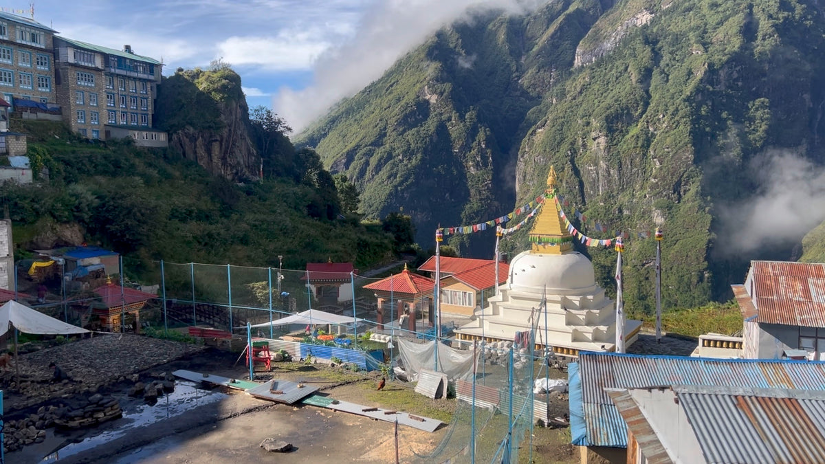 White Buddhist stupa strung with prayer flags below steep, forested Himalayan hillsides in Nepal